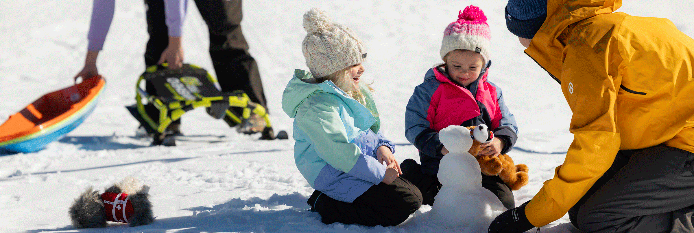 Two kids and a dad playing in the snow building a little snowman at Snow Valley